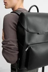 Mochila negra de cuero sintético con solapa y cierre magnético. Tiene un compartimento principal con espacio para dispositivos electrónicos de hasta 13 pulgadas y un bolsillo con cierre. En la parte frontal tiene un bolsillo con cierre y bolsillos planos en los laterales. La parte posterior es acolchada y tiene una banda de sujeción para equipaje. Tiene asa de mano y dos asas de hombro ajustables y acolchadas.