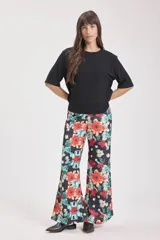 Pantalón palazzo de tela fluida con estampado floral en tonos naranja, celeste y blanco sobre fondo negro.