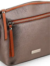 Bandolera color peltre con correa de cuero marrón regulable. Tiene un bolsillo externo con cierre y chapita metálica con el logo de la marca.
