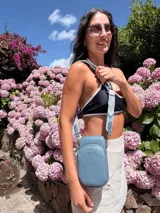 Bandolera pequeña tipo 'phone bag' de símil cuero color rosado pálido, con cierre de cremallera y correa ancha de tela con diseño de chevron en tonos claros.