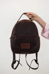 Mochila pequeña de cuero color marrón y beige, con bolsillo externo con cierre, manija superior, bolsillos laterales con broche imán y correas ajustables.