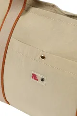 Bolso negro tipo tote con asas de hombro de cinta blanca. Tiene un bolsillo externo con botón a presión y cierre superior con cremallera.