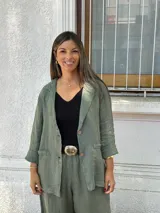 Blazer de lino color verde seco, de corte relajado y manga larga remangada. Presenta solapas anchas, cierre frontal con dos botones y bolsillos de parche.