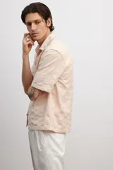 Camisa de manga corta color rosa claro, con cuello inglés, tapeta lisa, bolsillo superior abierto, canesú en la espalda y bajo recto.