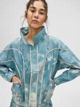 Campera rompevientos estilo biker con capucha desmontable, color celeste con estampado de nubes blancas y detalles en blanco.