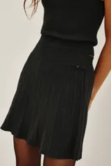 Minifalda negra tejida con cintura ancha elastizada y diseño plisado que genera movimiento.