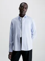 Camisa celeste de popelín de algodón elástico, corte slim, con cierre frontal de botones, mangas largas y monograma de Calvin Klein bordado en el pecho.