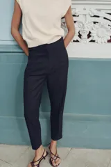 Pantalón largo negro con finas rayas verticales blancas, de tiro alto y corte recto.