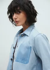 Campera de jean celeste claro, corte crop, con cuello clásico, cierre frontal con botones, mangas largas, dos bolsillos frontales y ruedo desflecado.