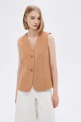 Chaleco color camel sin mangas, con cuello en V y cierre frontal con dos botones. Diseño con pinzas en la cintura para un calce entallado.