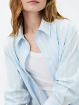 Camisa celeste con rayas verticales blancas, de manga larga y corte clásico.