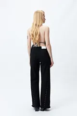 Pantalón de denim blanco con calce wide leg y ruedo desflecado. Presenta tachas metálicas a lo largo de los laterales.