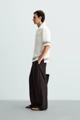 Pantalón marrón oscuro de corte amplio, confeccionado en mezcla de algodón y lino. Presenta cintura elástica, bolsillos laterales y trasero de parche, pliegues frontales, cierre con cremallera y botón.