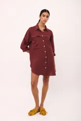 Vestido camisero corto color borgoña de lino italiano, con cuello camisero, manga larga, cierre frontal con botones y dos bolsillos de parche en el pecho con bordado de cerezas.