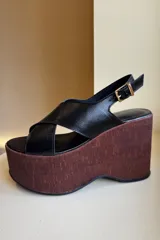 Sandalias de cuero negro con plataforma de madera color borgoña, con tiras cruzadas en el empeine y pulsera con hebilla al tobillo.