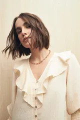 Camisa color crema a rayas verticales, con escote en V, mangas 3/4 con puños elásticos y volados en el frente.