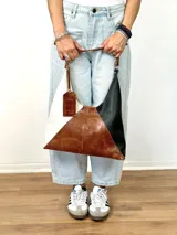 Bolso tipo hobo de cuero con diseño geométrico tricolor: blanco, marrón y negro.