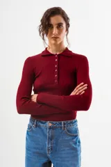 Top de tejido de punto acanalado color negro, de manga larga y cuello polo con botones frontales.