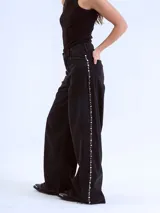 Pantalón de jean negro de corte wide leg con tachas plateadas en los laterales.