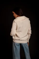 Buzo de punto color crema con cierre metálico y cuello alto.