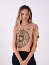 Remera corta de manga corta color marrón claro con un estampado circular de astrología y la frase "WE ARE THE FUTURE" en negro.
