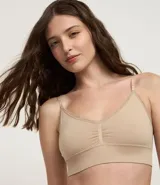 Soutien tipo top alargado color beige, confeccionado en tejido seamless de poliamida y elastano. Presenta breteles finos ajustables, relleno removible y un borde de encaje estrecho en el escote.