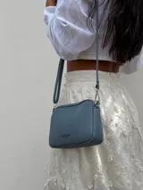 Bandolera pequeña de símil cuero color gris con textura granulada. Posee dos compartimientos principales con cierre y un bolsillo frontal con cremallera metálica. Incluye correa fina ajustable y extraíble.