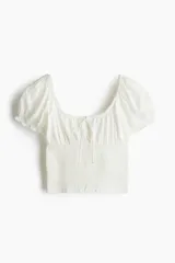 Blusa blanca de viscosa con escote cuadrado, mangas cortas abullonadas con elástico en hombros y puños, cintura fruncida y abertura con cordón en el delantero.