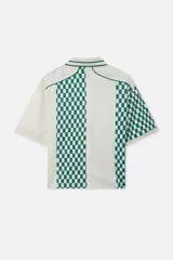 Remera tipo polo de manga corta color crema con estampado a cuadros verdes y blancos en el frente y mangas. Tiene cuello tipo polo con ribete verde, cierre con botones y logo de la marca bordado en el pecho.