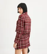 Campera corta de tweed a cuadros en tonos rojo, blanco y negro. Tiene cuello clásico, cierre frontal con botones, dos bolsillos en el pecho y flecos en el dobladillo.