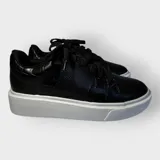Championes negros de cuero sintético con textura tipo piel de reptil, cordones anchos y suela plana.