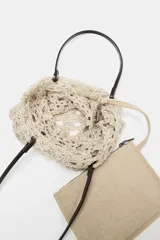 Bolso tipo shopper de tamaño pequeño, tejido en crochet color beige claro con patrón calado. Incluye asas de hombro de cuero sintético marrón oscuro y una bolsa interior con cierre de cremallera.