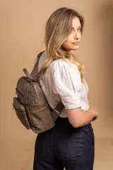 Mochila mediana color gris topo, de símil cuero con textura grabada. Tiene asa superior, dos compartimentos principales con cierre, dos bolsillos frontales con cierre y correas acolchadas ajustables.