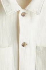 Sobrecamisa color crema en tejido texturizado de algodón, corte estándar, con cuello inglés, tapeta lisa, bolsillos superiores abiertos, canesú en la espalda, mangas largas con puños abotonados y bajo recto.
