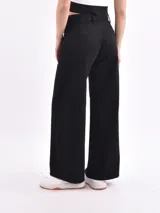 Pantalón de jean negro, tiro alto, de corte ancho (wide leg) y largo hasta el tobillo. Presenta cierre frontal con botón y bolsillos clásicos de jean.