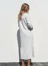 Vestido camisero blanco confeccionado en lino, de corte recto y largo midi. Presenta cuello camisero, mangas 3/4 con puños abotonados, cierre frontal con botones y abertura en el ruedo.