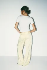 Pantalón cargo color blanco hueso, de tiro medio, corte ancho y tela satinada. Incluye cinturón con hebilla metálica, bolsillos delanteros, laterales con cierre y traseros de vivo. Cierre frontal con cremallera y ganchos metálicos.