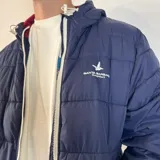 Campera inflada color ocre con capucha, cierre frontal con cremallera y logo de la marca bordado en el pecho.