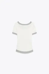 Camiseta blanca de corte slim fit, cuello redondo y manga corta con acabados en puntilla. Tiene detalle de frunces en los laterales y tejido combinado a contraste efecto doble en cuello, mangas y ruedo.