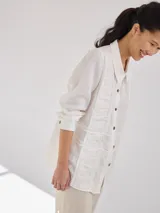 Camisa negra de lino con corte femenino, cuello clásico, cierre frontal con botones y mangas 3/4 con puños enrollados. Presenta detalles de frunces verticales en el frente y bolsillos de parche a la altura de la cadera.