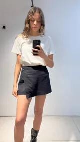 Short pollera negro de viscosa, poliéster y lino, con corte asimétrico y un botón decorativo.