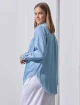Camisa de jean celeste con flecos en el ruedo, de mangas largas y corte recto.