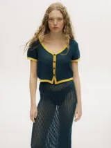 Top tejido calado color azul petróleo con cuello en V y botones carey. Tiene mangas cortas y puños en color amarillo contrastante.