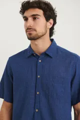 Camisa sport de manga corta color verde oliva, línea premium, con cuello clásico, cierre frontal con botones de coco y bolsillo de parche en el pecho. Confeccionada en lino y algodón.