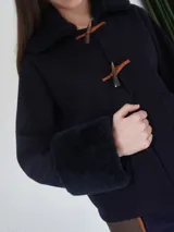 Campera corta negra con cuello y puños de piel sintética negra. Cierre con presillas de madera.