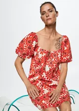 Vestido corto evasé de algodón con estampado de margaritas rojas, cuello cuadrado con lazo y mangas cortas abullonadas. Incluye forro interior y espalda abierta.