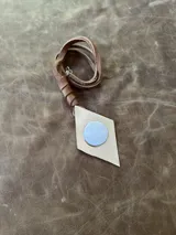 Collar con tiento de cuero marrón y dije en forma de rombo de alpaca con incrustación de nácar.