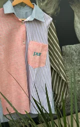 Camisa de manga larga con diseño patchwork a rayas horizontales en tonos celeste, naranja y verde. Tiene cuello clásico, bolsillo en el pecho y cierre con botones.