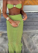 Conjunto de bikini negro con lunares blancos, compuesto por un corpiño bandeau con detalle de hebilla dorada y una falda larga de tul transparente con abertura lateral y lazos ajustables en la cadera.