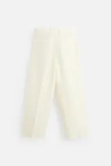 Pantalón color crema de lino, corte amplio, con pliegues frontales, bolsillos laterales y traseros de ojal. Cierre frontal con cremallera y gancho metálico oculto.